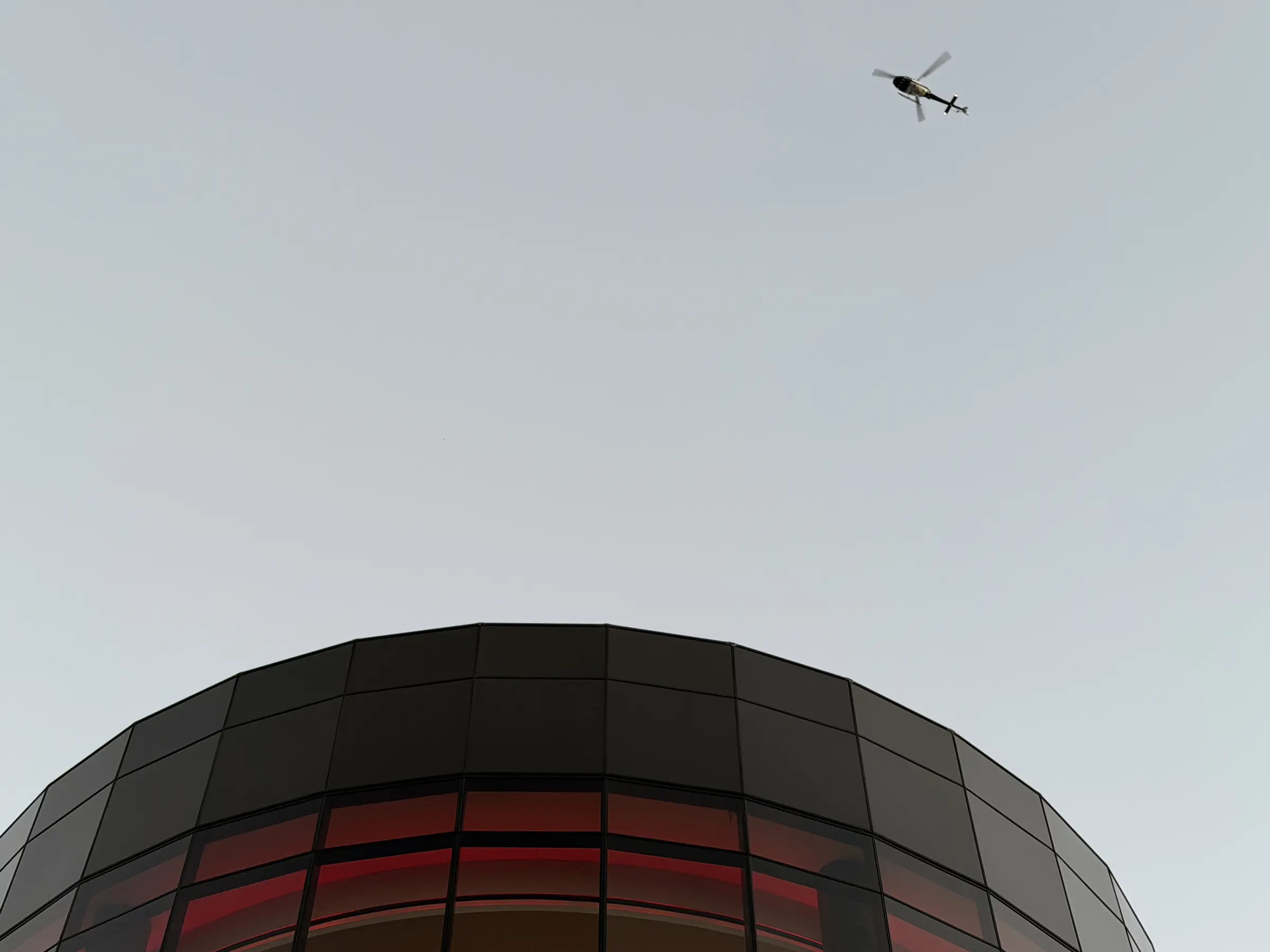 A helicopter passing over the curved glass crown of a tower